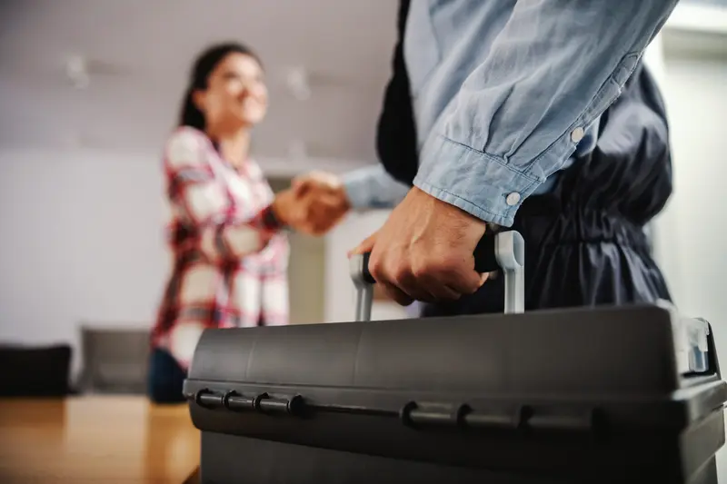 Plumber with a toolbox shaking hands with a homeowner